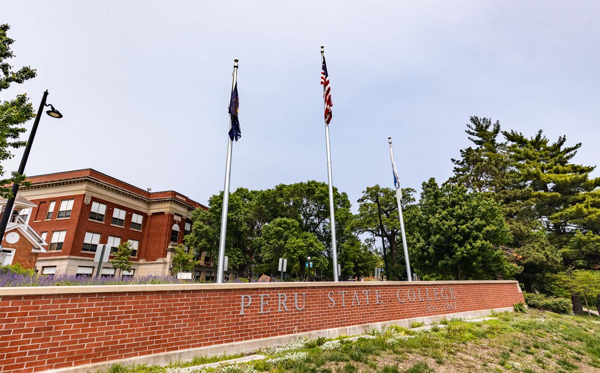 a sign for peru state college with flagpoles and flags